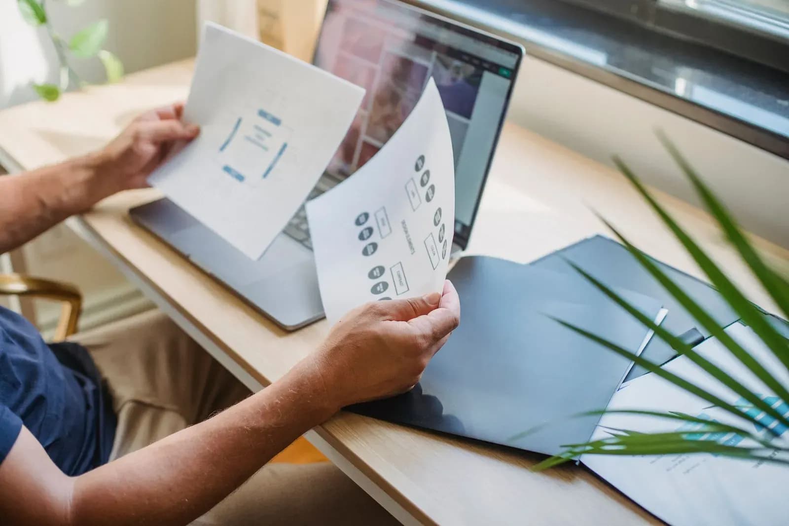 Designer web și client analizând schița unui site la cheie pe laptop, într-un birou luminos